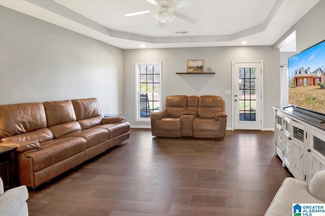 living area featuring a tray ceiling, dark wood finished floors, visible vents, and a healthy amount of sunlight