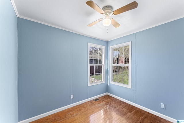 spare room with visible vents, a ceiling fan, ornamental molding, wood finished floors, and baseboards