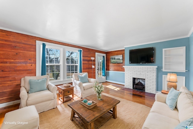 living room with built in features, ornamental molding, wood finished floors, wood walls, and a brick fireplace