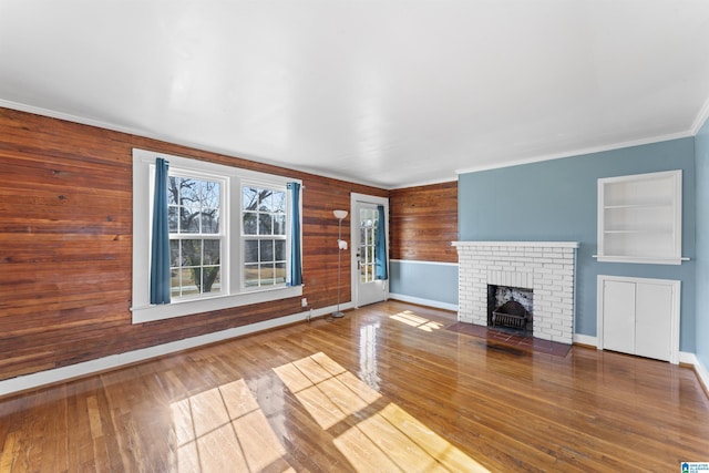 unfurnished living room with built in shelves, crown molding, a fireplace, and hardwood / wood-style flooring