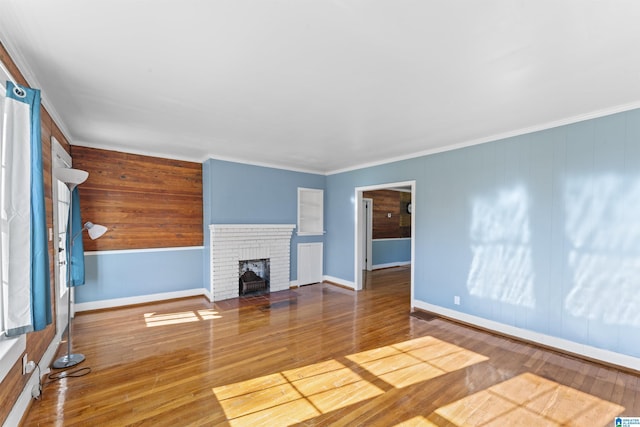 unfurnished living room with baseboards, a brick fireplace, wood finished floors, and crown molding