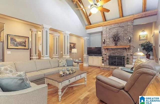 living room with decorative columns, ceiling fan, wood finished floors, a high ceiling, and a stone fireplace