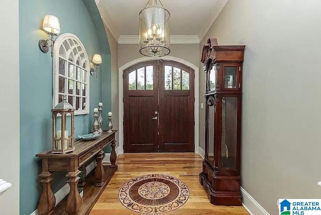 entryway with light wood finished floors, baseboards, arched walkways, ornamental molding, and a chandelier