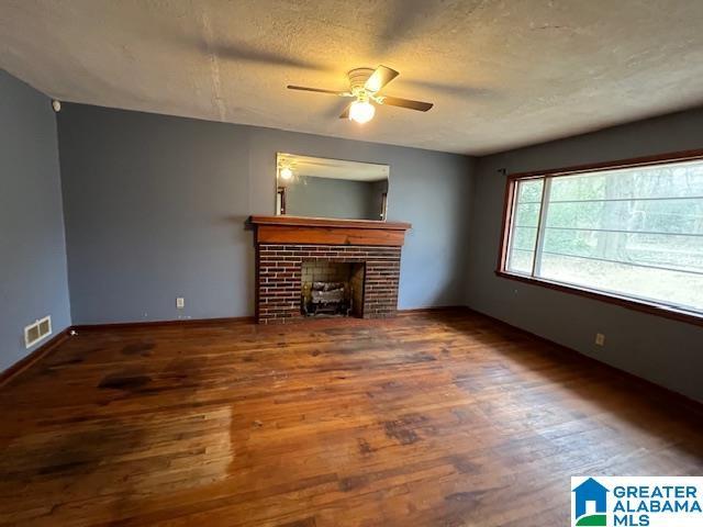 unfurnished living room with a textured ceiling, a fireplace, visible vents, and wood finished floors