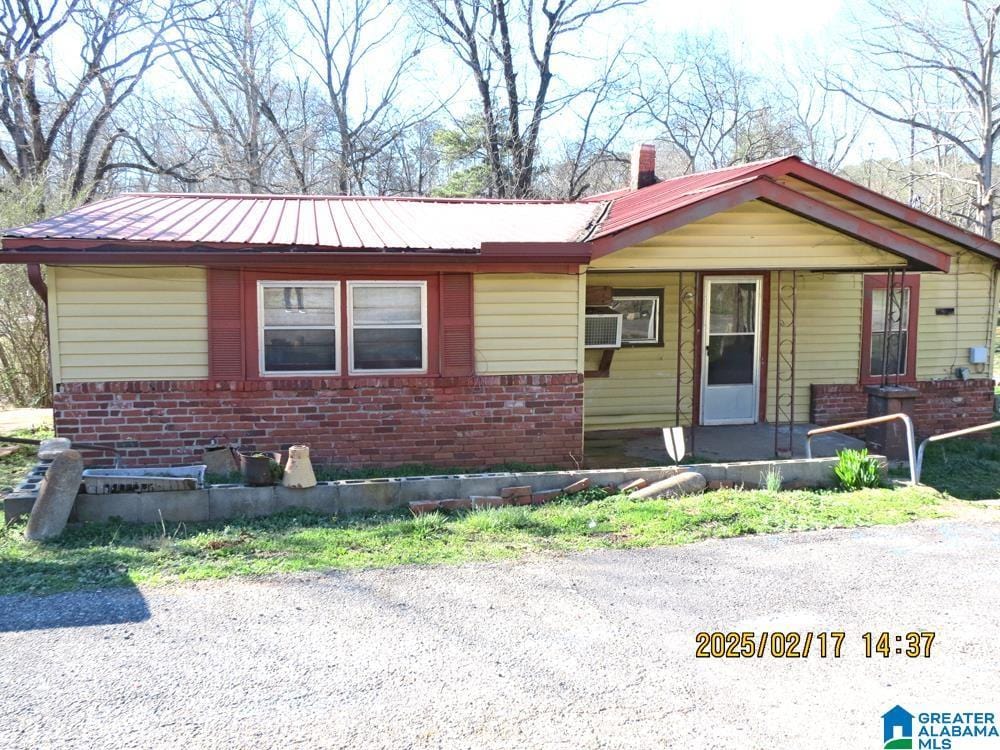 ranch-style home featuring covered porch, metal roof, brick siding, and a chimney