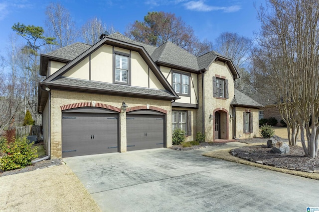 tudor house with driveway, a shingled roof, stucco siding, an attached garage, and brick siding