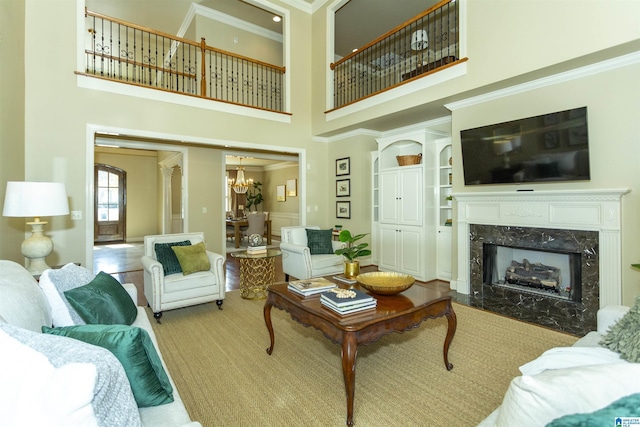 living room featuring a towering ceiling, a premium fireplace, ornamental molding, and a notable chandelier