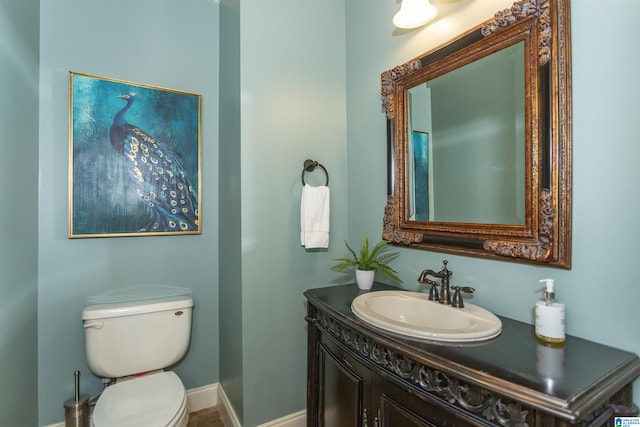 half bath with baseboards, vanity, and toilet