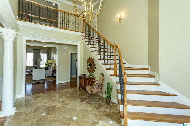 stairs featuring a towering ceiling, decorative columns, and baseboards