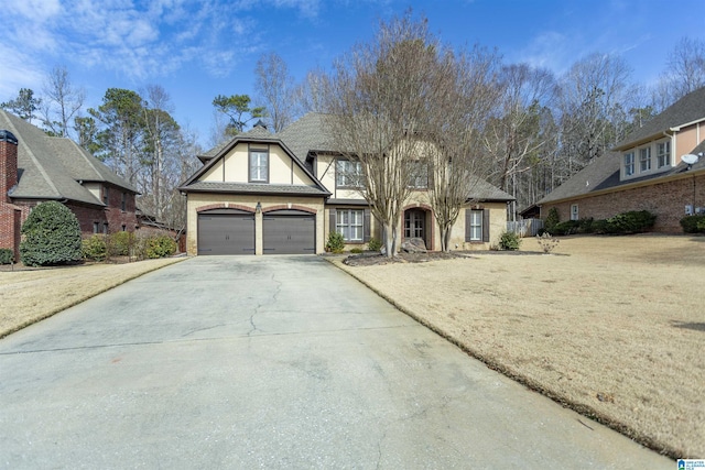 tudor house with driveway, an attached garage, a front yard, and stucco siding