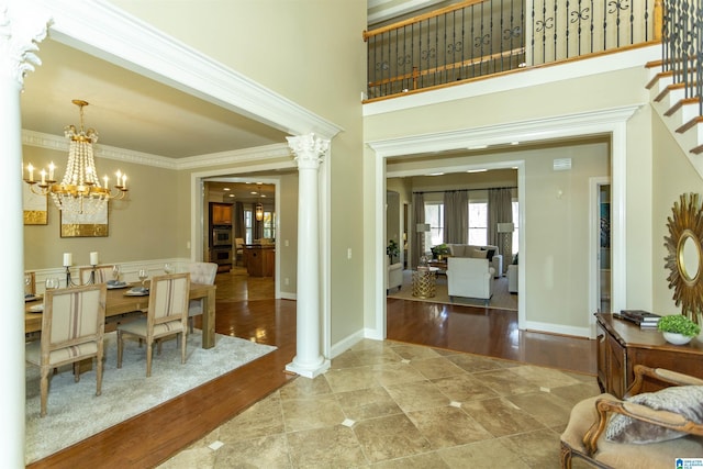 entrance foyer with ornamental molding, a towering ceiling, ornate columns, and wood finished floors