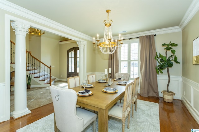 dining space with decorative columns, a wainscoted wall, stairway, wood finished floors, and crown molding