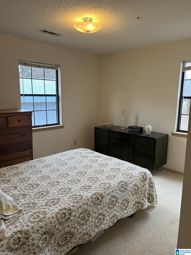 carpeted bedroom featuring a textured ceiling, visible vents, and baseboards