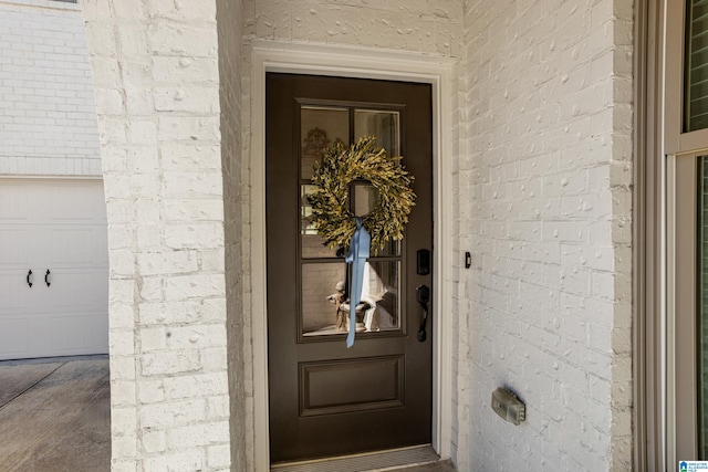 entrance to property featuring a garage and brick siding