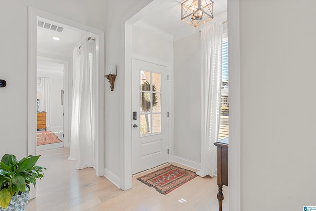 foyer featuring visible vents, baseboards, light wood-style floors, ornamental molding, and an inviting chandelier