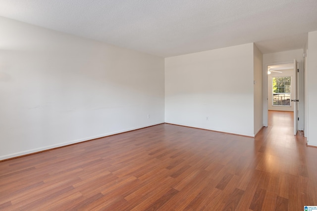 spare room with a textured ceiling, baseboards, and wood finished floors