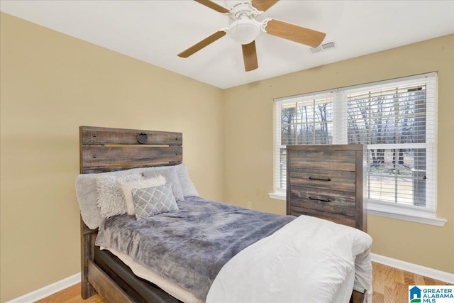 bedroom with ceiling fan, wood finished floors, visible vents, and baseboards