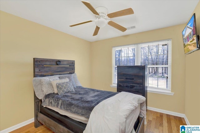 bedroom with a ceiling fan, visible vents, baseboards, and wood finished floors