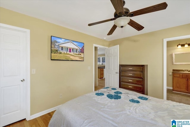 bedroom featuring ensuite bathroom, ceiling fan, wood finished floors, a sink, and baseboards