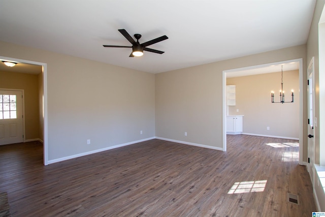 spare room featuring ceiling fan with notable chandelier, dark wood-type flooring, visible vents, and baseboards