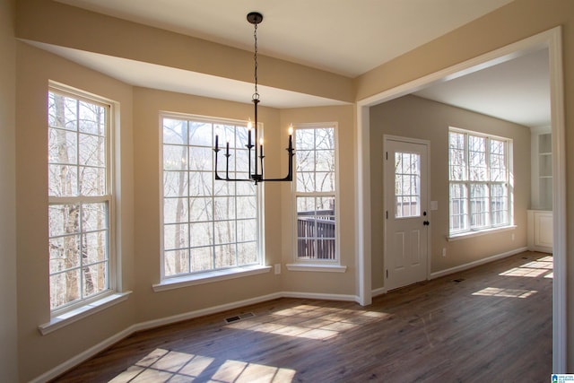 unfurnished dining area with an inviting chandelier, dark wood finished floors, visible vents, and baseboards