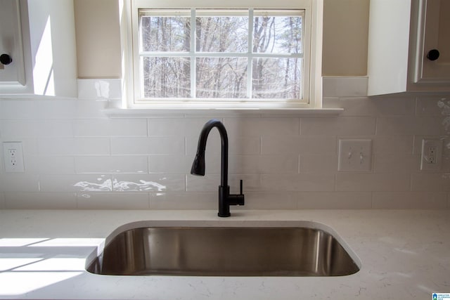 interior details featuring tasteful backsplash, a sink, and light stone countertops