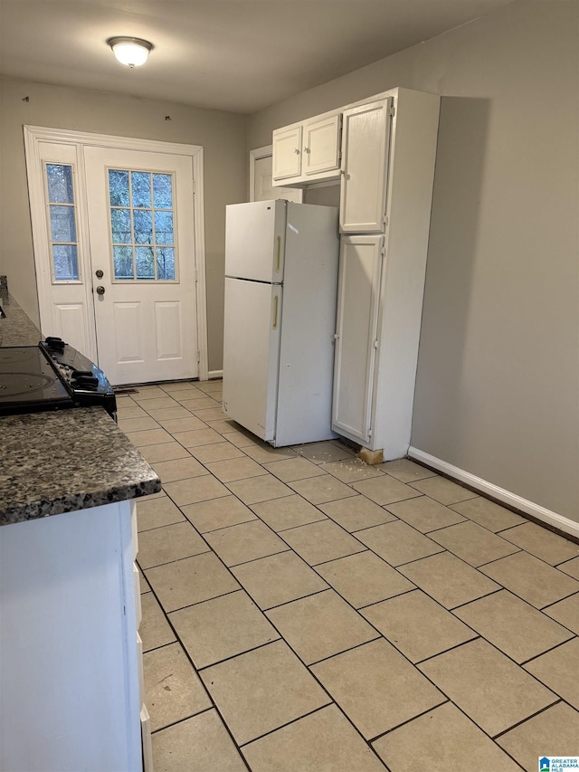 kitchen with dark countertops, freestanding refrigerator, white cabinetry, range, and baseboards