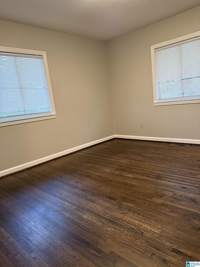 unfurnished room featuring visible vents, baseboards, and dark wood-type flooring