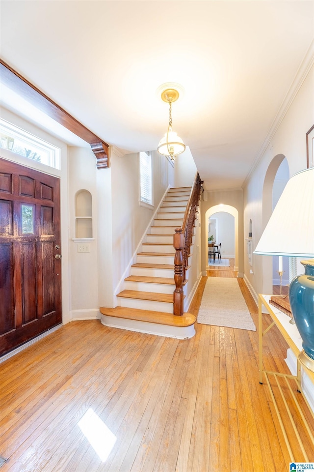 foyer entrance featuring arched walkways, hardwood / wood-style flooring, baseboards, ornamental molding, and stairway