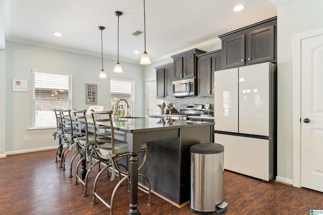 kitchen with dark wood-type flooring, a sink, stainless steel appliances, a breakfast bar area, and decorative backsplash