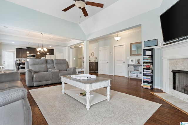 living room featuring lofted ceiling, a tiled fireplace, ceiling fan with notable chandelier, dark wood-style floors, and baseboards