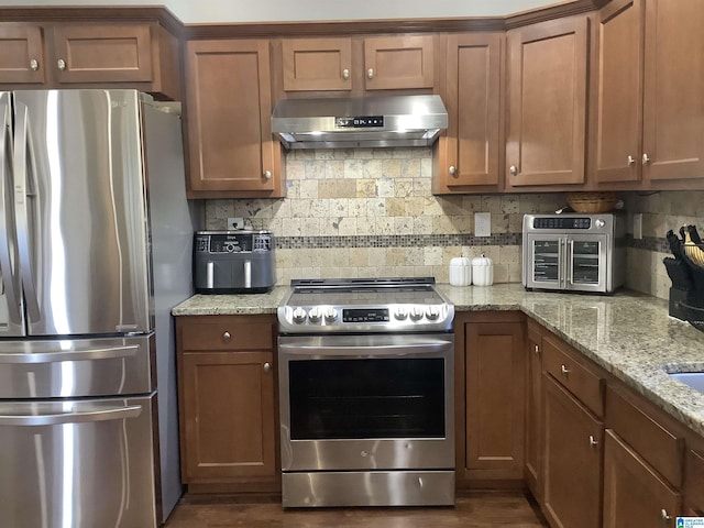 kitchen featuring brown cabinets, under cabinet range hood, tasteful backsplash, and stainless steel appliances