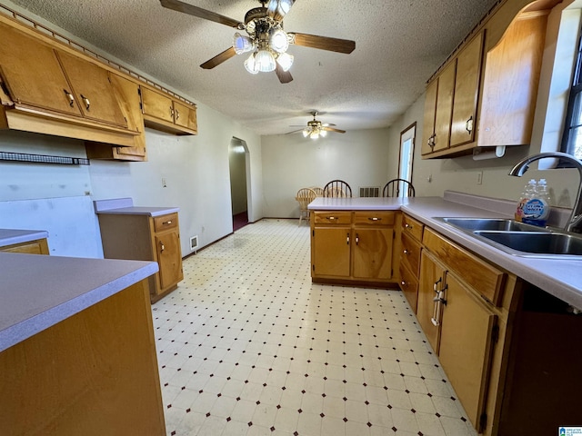 kitchen with brown cabinets, light floors, a sink, a textured ceiling, and a peninsula