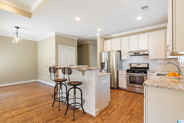 kitchen with light wood-style floors, a breakfast bar area, appliances with stainless steel finishes, under cabinet range hood, and a sink