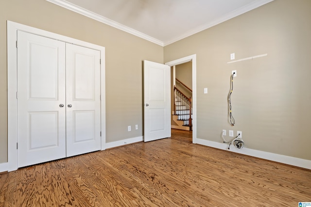 unfurnished bedroom featuring ornamental molding, a closet, baseboards, and wood finished floors