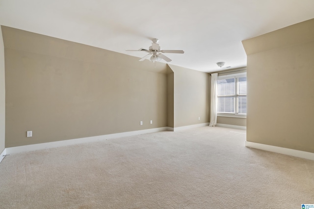 spare room with a ceiling fan, light colored carpet, and baseboards