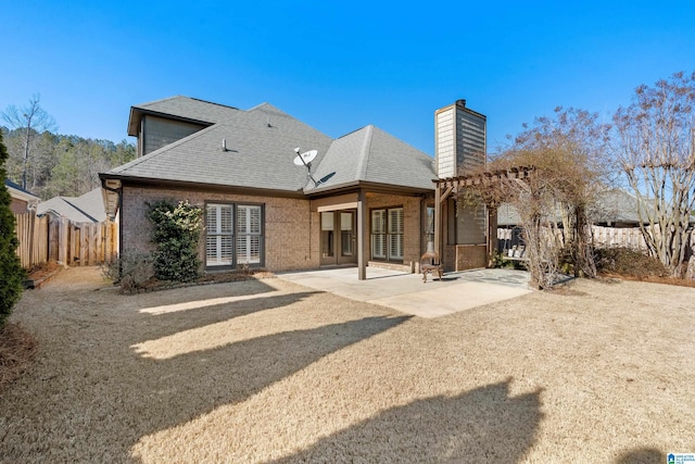 rear view of house featuring a patio, a chimney, roof with shingles, fence, and brick siding