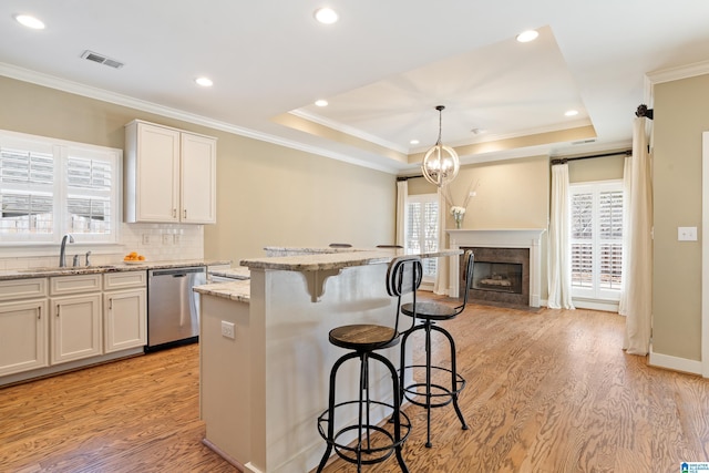 kitchen featuring visible vents, a breakfast bar area, a tray ceiling, stainless steel dishwasher, and a sink