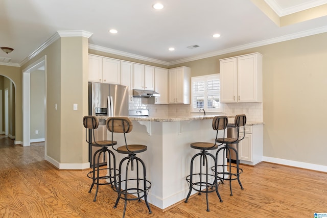 kitchen with arched walkways, stainless steel refrigerator with ice dispenser, light wood finished floors, white cabinetry, and a kitchen bar