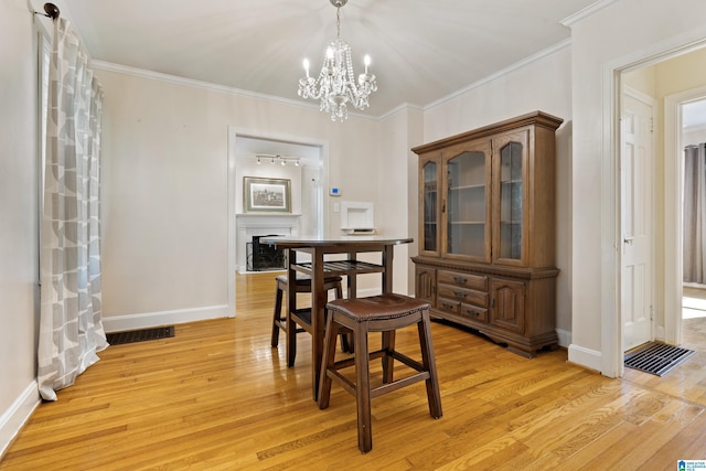 dining area featuring ornamental molding, light wood-type flooring, and a fireplace