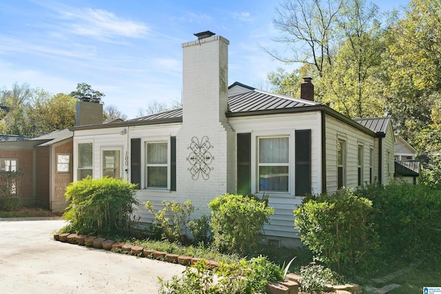 view of property exterior with metal roof, brick siding, a standing seam roof, and a chimney