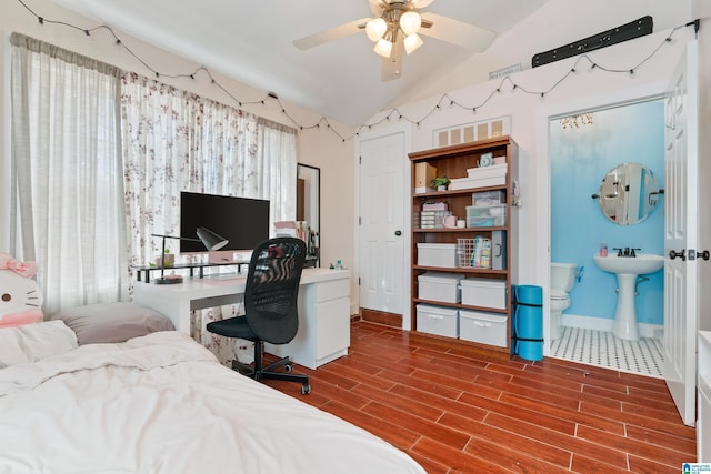 bedroom featuring wood finish floors, lofted ceiling, connected bathroom, a sink, and baseboards