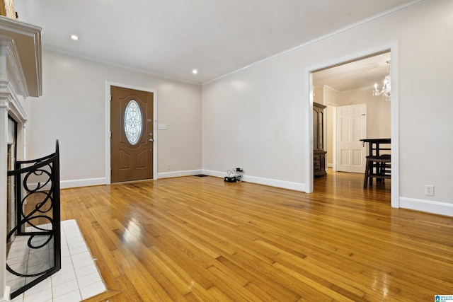 foyer with a fireplace, baseboards, ornamental molding, light wood finished floors, and an inviting chandelier