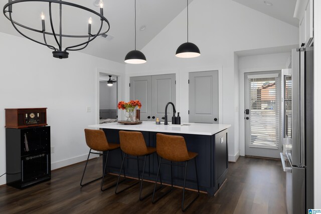 kitchen with a center island with sink, light countertops, dark wood-type flooring, freestanding refrigerator, and a sink