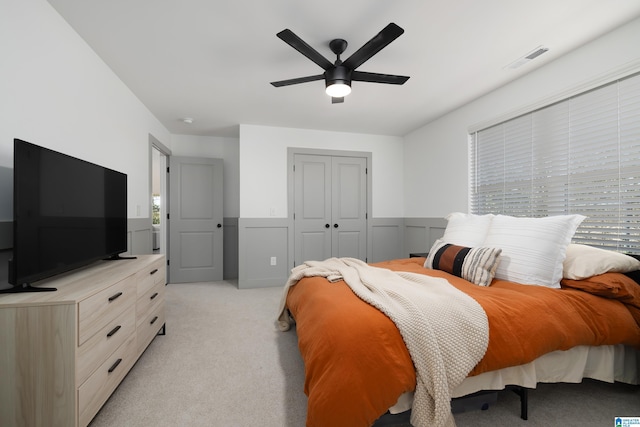 bedroom with light colored carpet, a ceiling fan, visible vents, a closet, and wainscoting