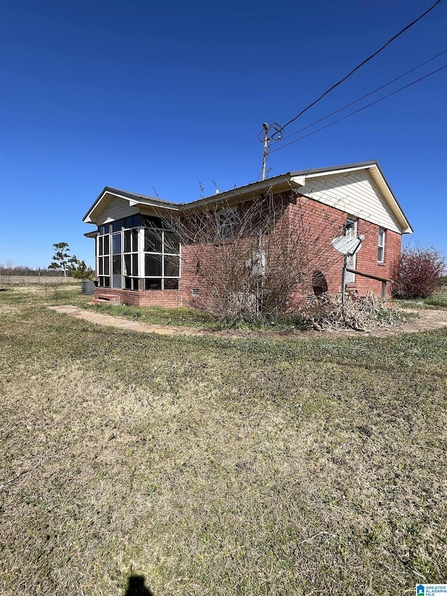 back of property featuring a sunroom, brick siding, and a lawn