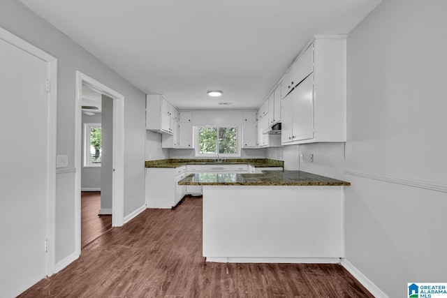 kitchen featuring under cabinet range hood, a peninsula, dark wood-type flooring, baseboards, and white cabinets