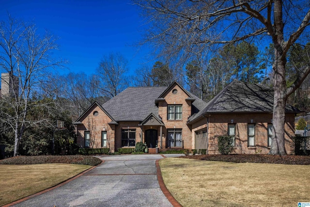 view of front of house featuring driveway, brick siding, a front yard, and a shingled roof