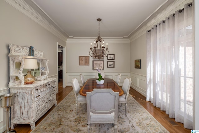 dining room with crown molding, wainscoting, a notable chandelier, and wood finished floors