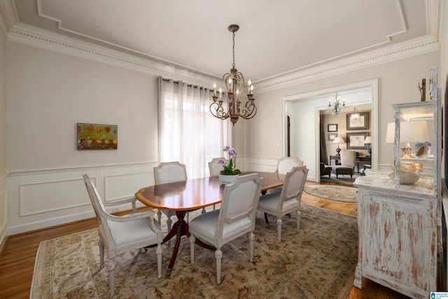 dining space featuring a wainscoted wall, a notable chandelier, a decorative wall, ornamental molding, and wood finished floors